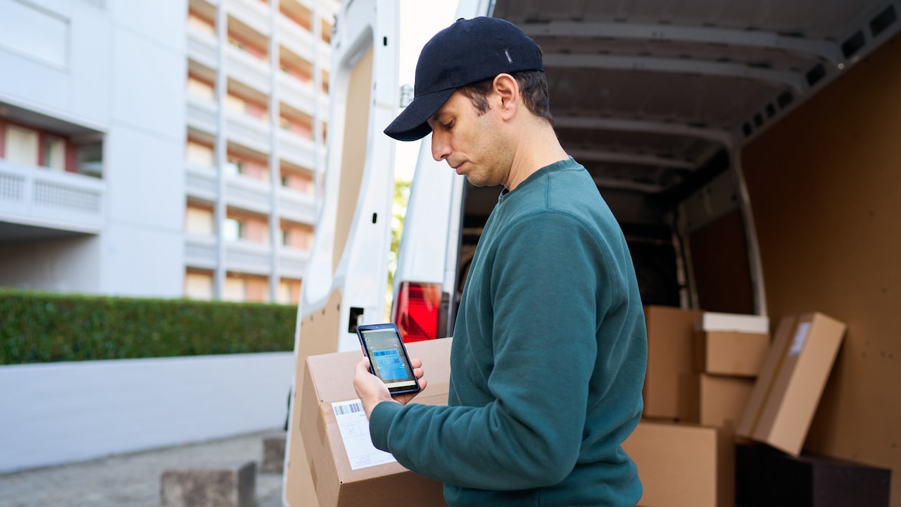 Delivery man scanning a parcel in front of the van